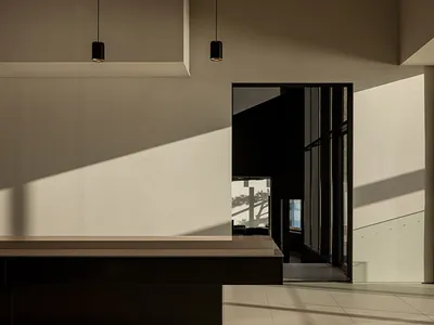 A modern dining space with a concrete wall, a dining table, chairs, and a couch, lit by natural light from a window