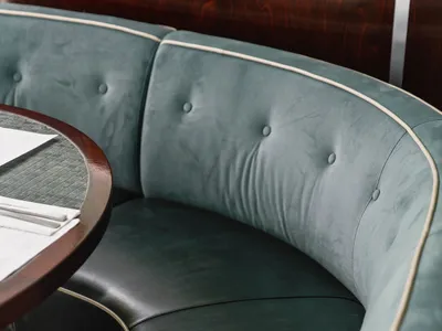 A cozy living room with a large green leather sofa, two chairs, and a dining table in the background, with a book on the table