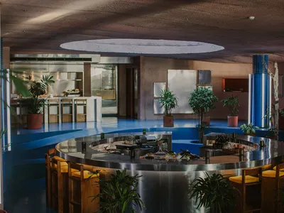 A modern restaurant with a circular dining table, potted plants, and brown walls creating a warm atmosphere