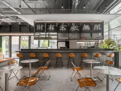 Modern Asian restaurant with grey walls, black accents, dining tables, chairs, and a bar area, well-lit with natural and artificial light