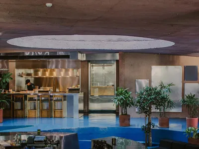 Modern restaurant interior with a circular bar, wood accents, metal elements, and potted plants, creating an inviting and comfortable atmosphere
