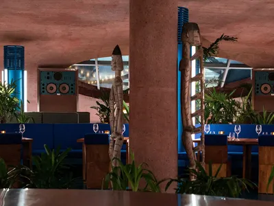 Warm-toned dining space with wooden posts, tables, chairs, and potted plants, creating a cozy atmosphere
