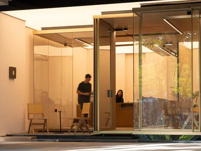 Casual dining area with wooden floor, chairs, and tables, well-lit with two people present
