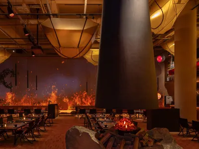 Warm and inviting dining space with multiple tables, chairs, and a fireplace, well-lit for a pleasant ambiance