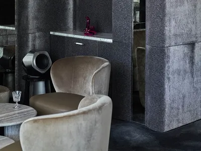 A cozy living room with a large mirror, two chairs, wine glasses, and a clock, set against a neutral background
