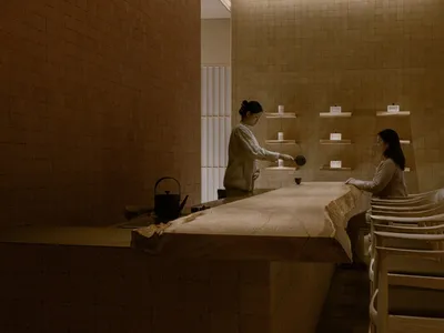 A woman cooks in a cozy kitchen with a wooden countertop, dining table, and various kitchen items, creating a warm and inviting atmosphere