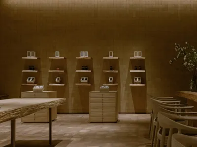 A welcoming interior design showroom with wooden floors and walls, featuring chairs, tables, and potted plants, with bottles on display