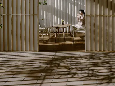 A well-lit indoor living space with a woman sitting on a chair near a dining table, surrounded by wooden furniture and a vase, creating a cozy atmosphere