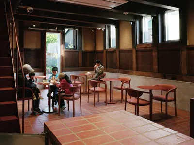 A casual dining area with multiple tables and seating options, including benches and chairs, with people gathered together