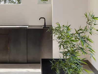 A well-lit bathroom with a sink, two potted plants, and natural light from windows