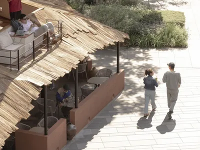 Outdoor restaurant with a thatched roof, tables, and chairs, surrounded by people dining and socializing