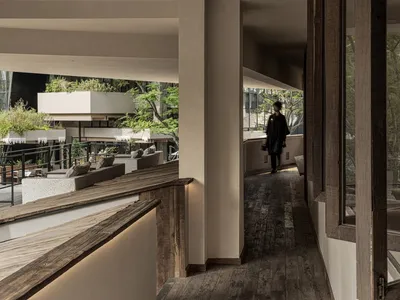 A warm and inviting hotel hallway with wooden flooring and walls, featuring chairs for seating and a person walking down the hall