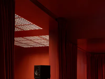 Cozy living space with orange walls, red curtains, a couch, two chairs, and two speakers for a relaxing atmosphere