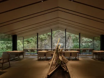 Open modern restaurant interior with tables, chairs, potted plants, and artwork on the walls