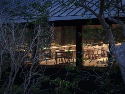 A dimly lit restaurant dining area with multiple tables and chairs, predominantly made of wood, creating a warm and inviting atmosphere