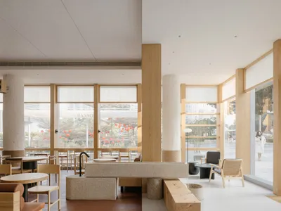 Open modern restaurant interior with wood flooring, chairs, and dining tables, well-lit with natural and artificial light