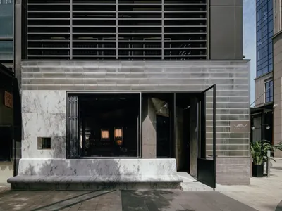A modern restaurant entrance with a black doorway featuring a glass window, allowing natural light to enter, and comfortable seating for guests