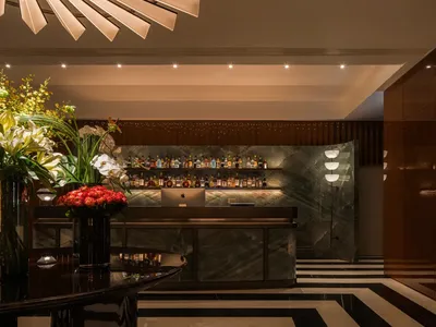 A luxurious hotel lobby bar with a marble countertop, glassware, and decorative vases, set against a neutral background
