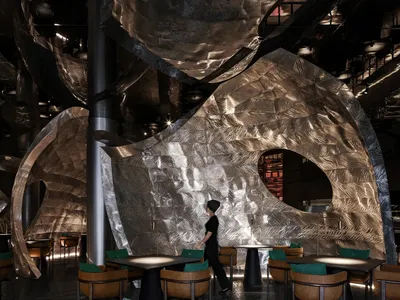 Modern restaurant interior with tables, chairs, and a bar, featuring metallic elements and a contemporary design
