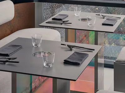 Modern dining space with tables, chairs, and glassware, set with black napkins and silverware, in a clean and minimalistic design