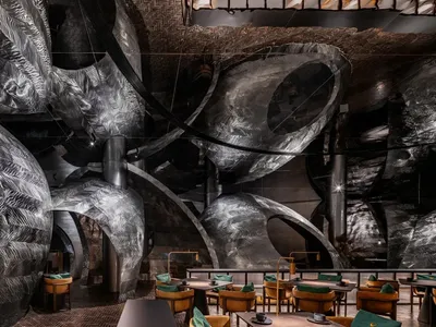A modern restaurant interior with a large dining area featuring intricate wall designs, multiple tables, and various seating options, including benches and chairs
