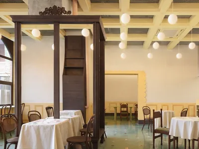 Dining area with multiple tables and chairs, warm tones on the walls, mixed flooring, and potted plants
