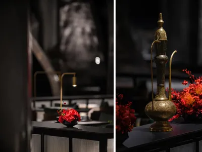 A warm and inviting dining space with a wooden table, gold accents, and decorative elements, featuring a vase with red flowers on a black table in the foreground and a well-designed dining area in the background