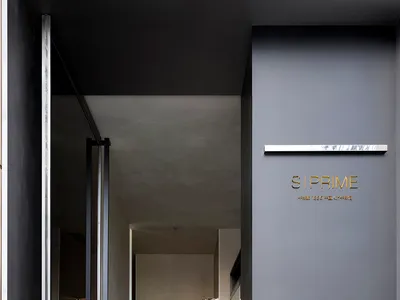 A modern hotel hallway with concrete walls, two open doors, and a yellow light adding warmth to the space