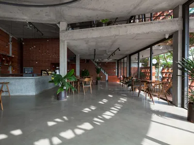 Modern restaurant interior with a large cement wall, concrete floor, and potted plants, featuring a minimalist and functional atmosphere