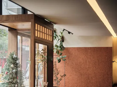Modern restaurant interior with a dining area, bar counter, and potted plants, featuring red brick walls and a warm atmosphere