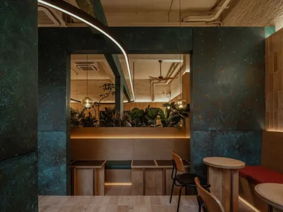 Modern restaurant interior with marble walls, tables, chairs, and a bar counter, surrounded by potted plants