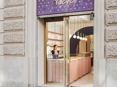 A bakery shop with a pink door, cakes on display in the window, and two women standing near the counter