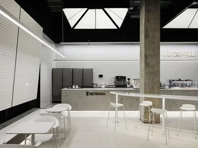 Modern restaurant interior with white walls, grey floors, and dining tables, chairs, and appliances