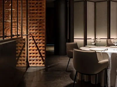 Sophisticated dining space with a large table, chairs, and wine glasses, surrounded by a brick wall and modern classic design elements
