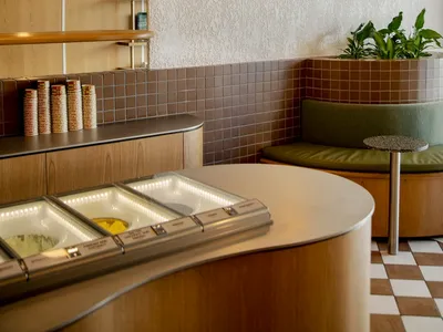 Modern restaurant interior with a counter, dining table, chairs, potted plants, and cups, featuring a welcoming atmosphere