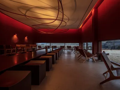 A modern restaurant lounge with a dining table, chairs, couches, and red walls, creating a comfortable and inviting atmosphere for socializing and dining