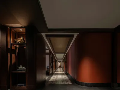 A long, well-lit hotel hallway with red walls, chairs, and a sense of depth and spaciousness
