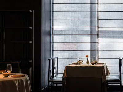 Dimly lit dining area with a table set for two, chairs, and a vase with flowers, creating a cozy atmosphere