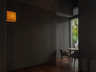 Cozy interior space with wooden walls and floors, featuring a dining table, chairs, and a potted plant