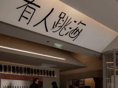 Casual modern restaurant with a bar featuring stools and tables, bottles on display, and a contemporary design