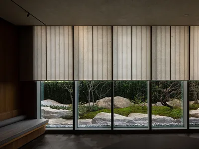A hotel living area with large windows, vertical blinds, and potted plants, offering a calm and inviting atmosphere with a focus on the connection between interior and exterior spaces