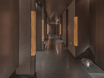 A calm and inviting empty hallway with a wooden floor and ample lighting from multiple fixtures on both sides