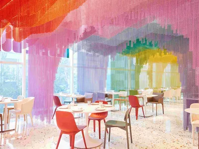 A modern restaurant dining area with multiple tables and chairs in various colors, including a pink chair, set in a comfortable and inviting space