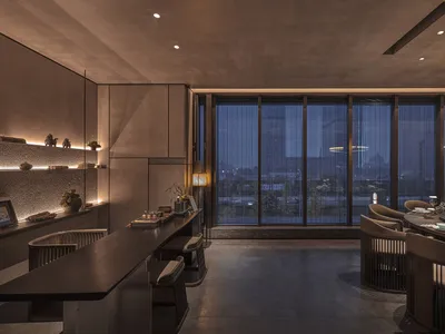 A modern restaurant interior with a large window offering a city view, featuring a dining table and chairs, potted plants, and a welcoming atmosphere