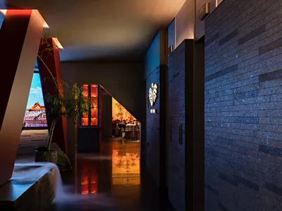 A modern hotel lobby with a large open area, a waterfall, and potted plants, featuring a dining table and stylish design