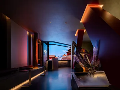 A modern hotel lobby with a mix of red and white elements, featuring potted plants and a vase, set in a spacious area with natural light from a large window