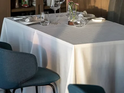 Elegant dining area with a white tablecloth, wine glasses, and dinnerware, surrounded by bottles and two chairs