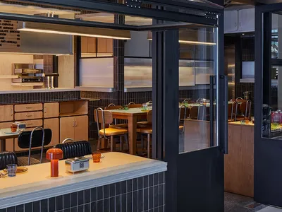 A modern restaurant with black tile walls, multiple dining tables, and chairs, with cups on some tables