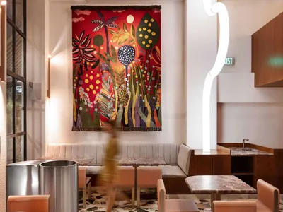 A cozy restaurant interior with a large painting on the wall, dining tables, and chairs, creating a warm atmosphere for guests