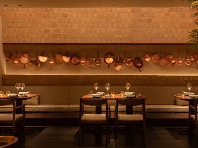 A warm and inviting dining space with multiple tables, chairs, wine glasses, and hanging pots, perfect for a relaxing meal